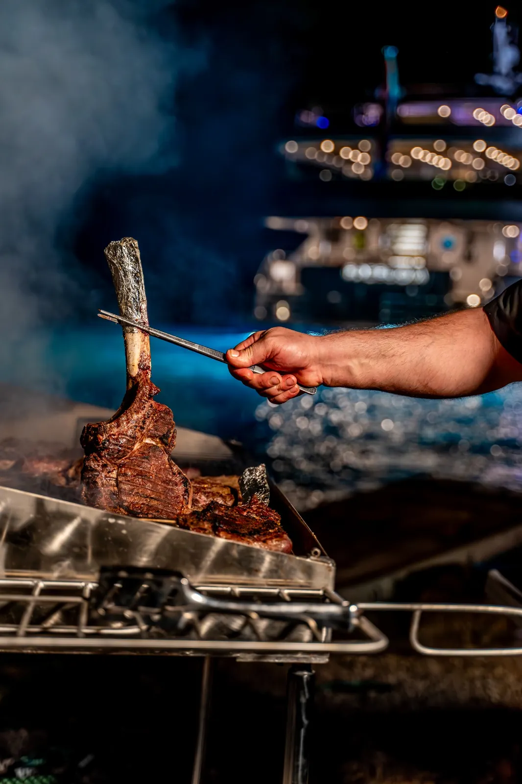 A chef of a crewed Croatia yacht charter preparing steak on shore while the yacht is anchored.
